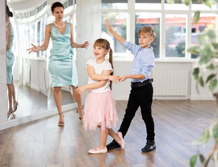 Boy and girl in pair train to dance waltz during classes. Children rehearse contemporary dancing movement. Female teacher conducts class for students