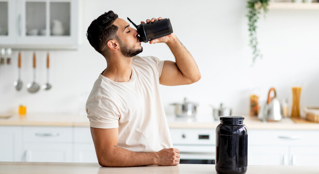 Young Arab guy drinking protein shake from bottle at kitchen, copy space. Millennial Eastern man using meal replacement for weight loss, having sports supplement for muscle gain. Body care concept