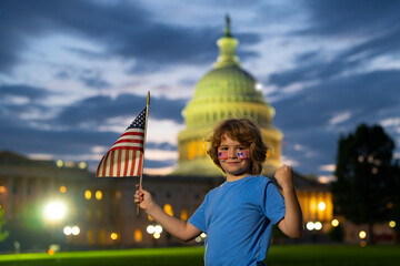 American Patriotic holiday. American kid, cute little child boy with American flag near Capitol...