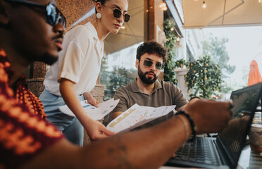 Diverse businesspeople collaborating outdoors, reviewing documents and laptop, working together in a casual setting. Teamwork and communication depicted through discussion and sharing ideas.