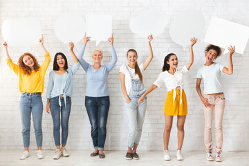 Fototapeta premium Female Group Opinion. Smiling Multiracial Ladies Holding Empty Speech Bubbles Standing Over White Brick Wall Indoors. Mockup