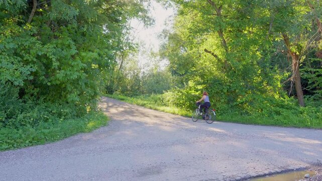 A young red-haired woman is turning the corner upwards a hill on a bicycle spending her weekend in green beautiful nature in the countryside of Maribor, Slovenia, casual outfit, dynamic