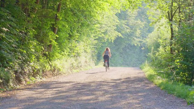 A young red haired woman cycling up the hill in casual outfit on a summers day in Slovenia Maribor, active, outdoors, struggle, dynamic, ordinary, green, sunny