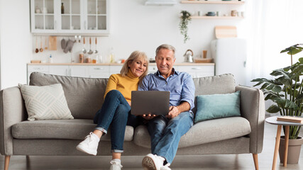 Senior Spouses Using Laptop Watching Movie Together Sitting On Couch At Home. Older Couple Browsing...