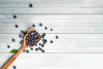 Fresh, ripe blueberries spilling out of a wooden scoop onto a wooden table with copy space.