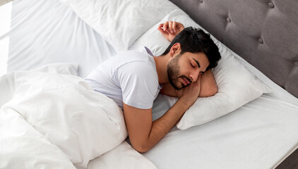 Asleep young arab man sleeping, resting peacefully in comfortable bed, lying with closed eyes, free space. Recreation, deep male sleep, time to rest and nap concept