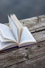 Pages of an open book on the wooden deck on the lake in the forest. Concept of reading, relaxing, meditating, education, visiting libraries, book exhibitions. Close up. Side view. Selective focus