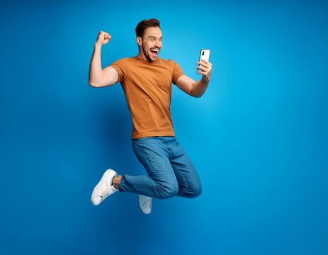 A man is jumping in the air with his arms raised and a cell phone in his hand