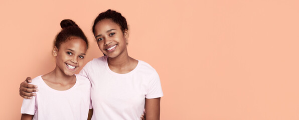 Cute little african sisters embracing over pink studio background