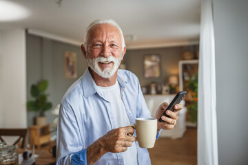 Senior man sit at kitchen drink coffee and hold cellphone and have fun