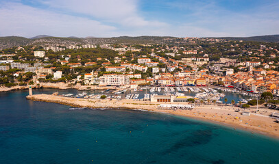 Scenic drone view of coastal small French town of Cassis overlooking port with moored yachts on sunny day .