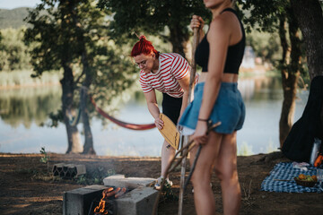 Two friends having a relaxing picnic by the lake. They are tending to a campfire, enjoying the outdoors, and spending time in nature.