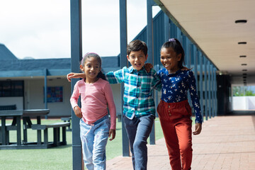 Obraz premium Three biracial children are walking together, smiling, in school