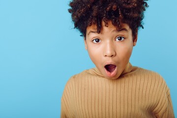 Astonished young african american girl with wide open mouth and surprised expression against a solid blue background