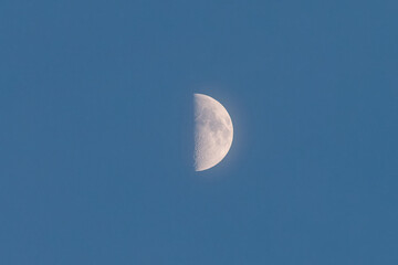 Close up view of half moon on blue sky background, telephoto lens shot.
