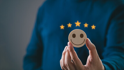 Hand holding a happy face coin with five stars above, representing excellent customer satisfaction...