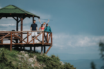 A group of friends stands at a wooden gazebo on a mountain, enjoying the scenic view on a clear day.