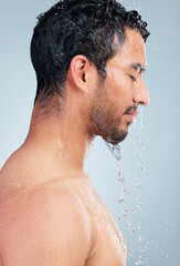 Man, water and shower for body care in studio, bathroom and grooming on blue background. Male person, peace and liquid for skincare in profile, cosmetics and washing for hygiene or facial treatment