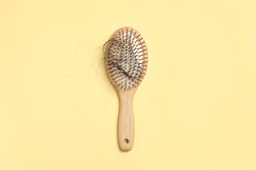Wooden brush with lost hair on yellow background, top view