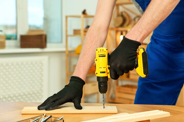 Craftsman working with drill at wooden table in workshop, closeup