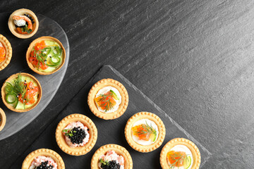 Delicious canapes with salmon and caviar on black textured table, flat lay. Space for text