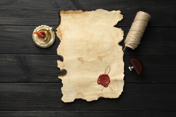Sheet of old parchment paper with wax stamp, twine and candle on black wooden table, top view