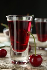 Shot glass of delicious cherry liqueur and juicy berry on wooden table, closeup