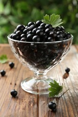 Ripe black currants and leaves in glass on wooden table, closeup