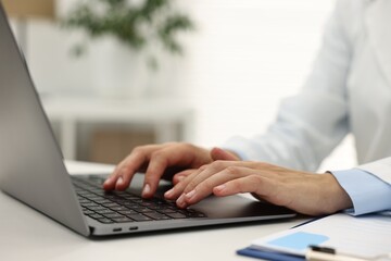 Doctor using laptop at white table in hospital, closeup