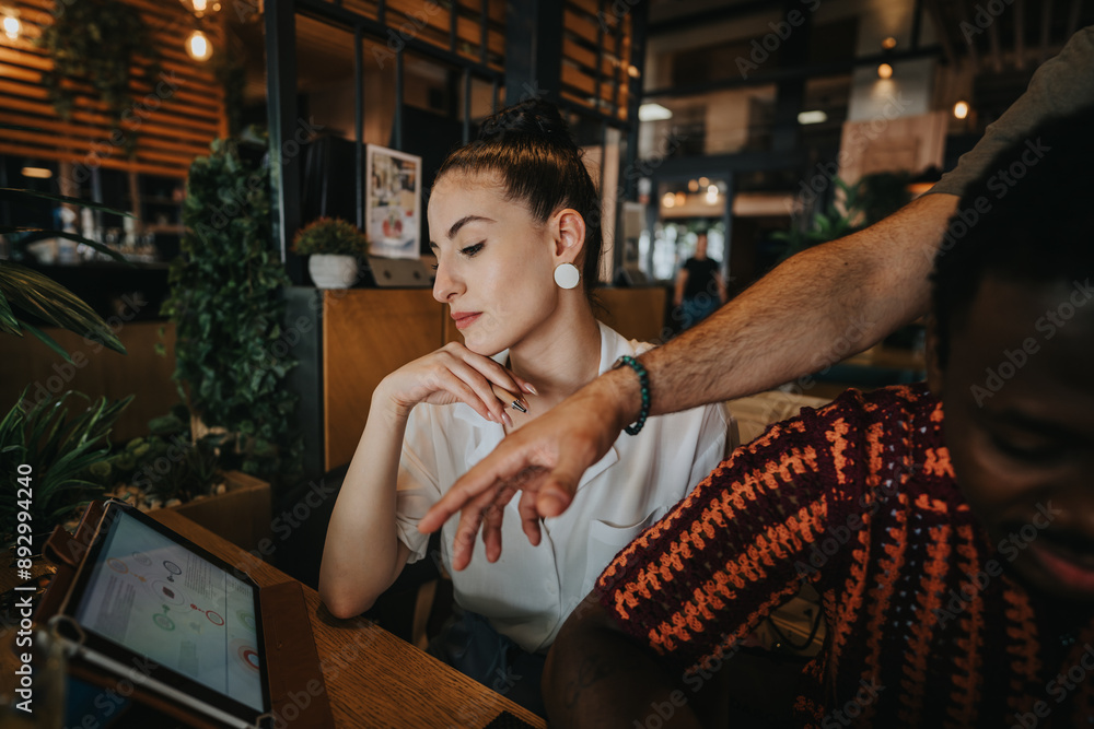 Wall mural Diverse individuals collaborating in a relaxed coffee bar setting, working together on a tablet during a meeting.