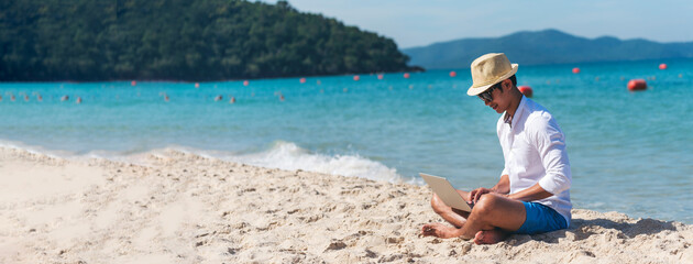 Banner Man traveler use laptop on summer beach blue sky. Asian man travel relax sitting summer...