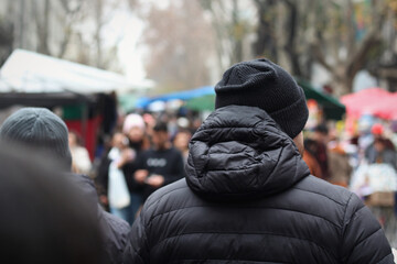 Homem de costas vestindo casaco preto e gorro de lã caminhando entre grupo de pessoas em día de inverno