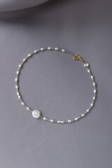 Beautiful pearl beaded necklace on gray textile backgound. Stylish accessory. Elegant white pendant jewelry flat lay