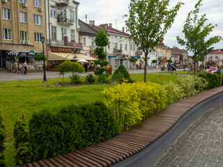 A welcoming scene of a wavy wooden bench positioned on a city sidewalk, providing a charming and tranquil spot for relaxation next to a lush expanse of vibrant green grass.