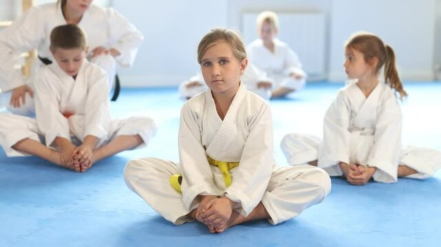 Boys and girls athletes before training martial arts performs stretching butterfly exercise in presence of experienced instructor. Preparation for competitions