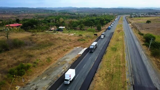 Panoramic aerial shot of a highway in the middle of nowhere with a group of trucks of various sizes moving one after another - 2.7K