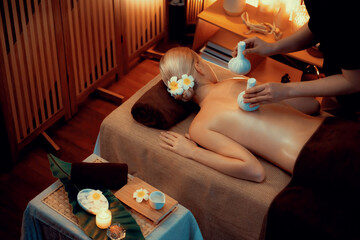 Hot herbal ball spa massage body treatment, masseur gently compresses herb bag on woman body....