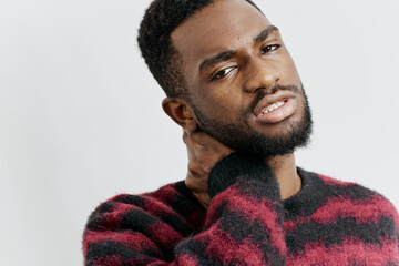 Young man in a red sweater looking thoughtful with his hand resting on his neck against a neutral...