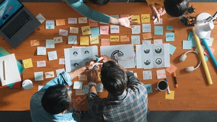 Top down aerial view of skilled designer hold logo while discuss with team. Aerial business group...