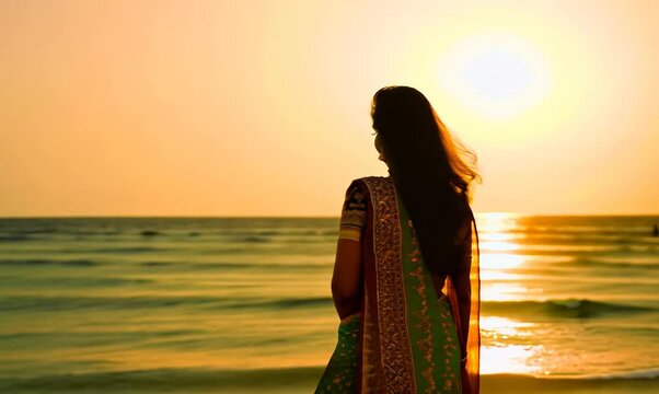 Beautiful indian woman in saree on the beach at sunset