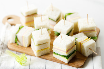 Sandwich of white soft bread with ham, cheese and lettuce on wooden board.