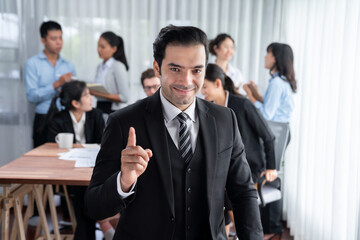 Portrait of happy businessman looking at camera, making finger pointing gesture for advertising product with motion blur background of business people movement in dynamic business meeting. Habiliment