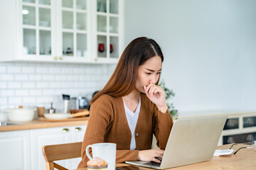 Asian young woman seriously working on computer laptop in house. She thinking find solution problem...