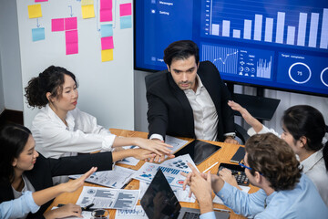 Wide top view of diverse group of business analyst team analyzing financial data report paper on meeting table. Chart and graph dashboard by business intelligence analysis. Meticulous