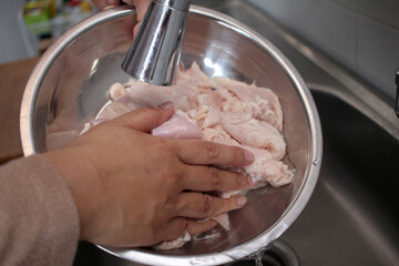 Asian muslim woman washing and cleaning chicken meat after cutting. Meal preparation