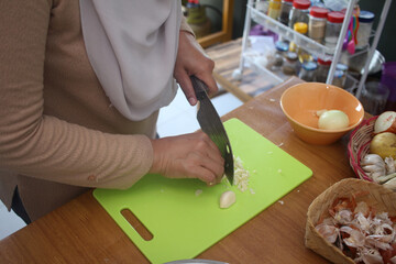 Asian muslim woman peeling, cutting and slicing onion and garlic. Preparing marinade for chicken meat