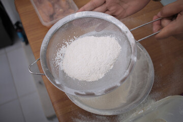 Asian muslim woman sifting flour to make spiced breaded chicken or bread baking