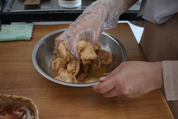 Close up of a person hand marinating chicken meat in metal bowl