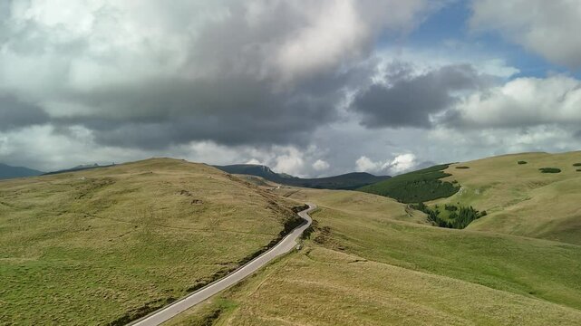 Aerial drone view of  Transbucegi road in Bucegi national park, Carpathian mountains, Romania in a cloudy summer day. Curvy asphalt road passing trough green hills and valleys
