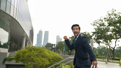 Dancing business man walking and hold bag while dancing at park. Happy funny project manager moving body to music while going to work. Happy man getting promotion, receive good news. Exultant.